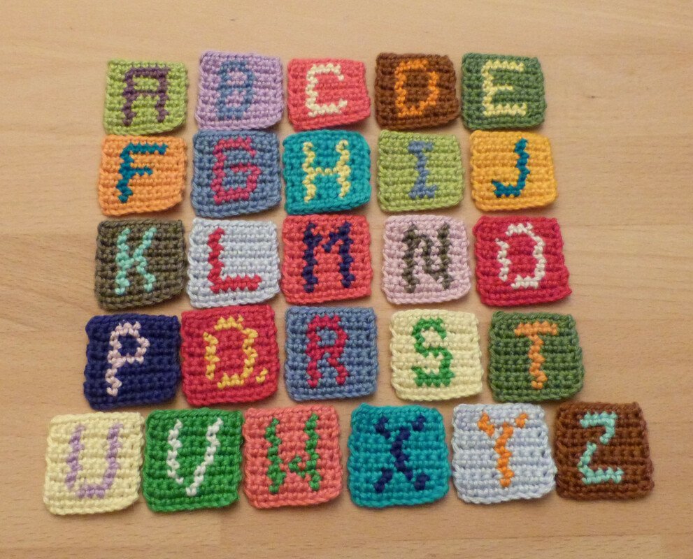 26 gehäkelte bunte Quadrate mit den Buchstaben A bis Z auf hellem Holztisch