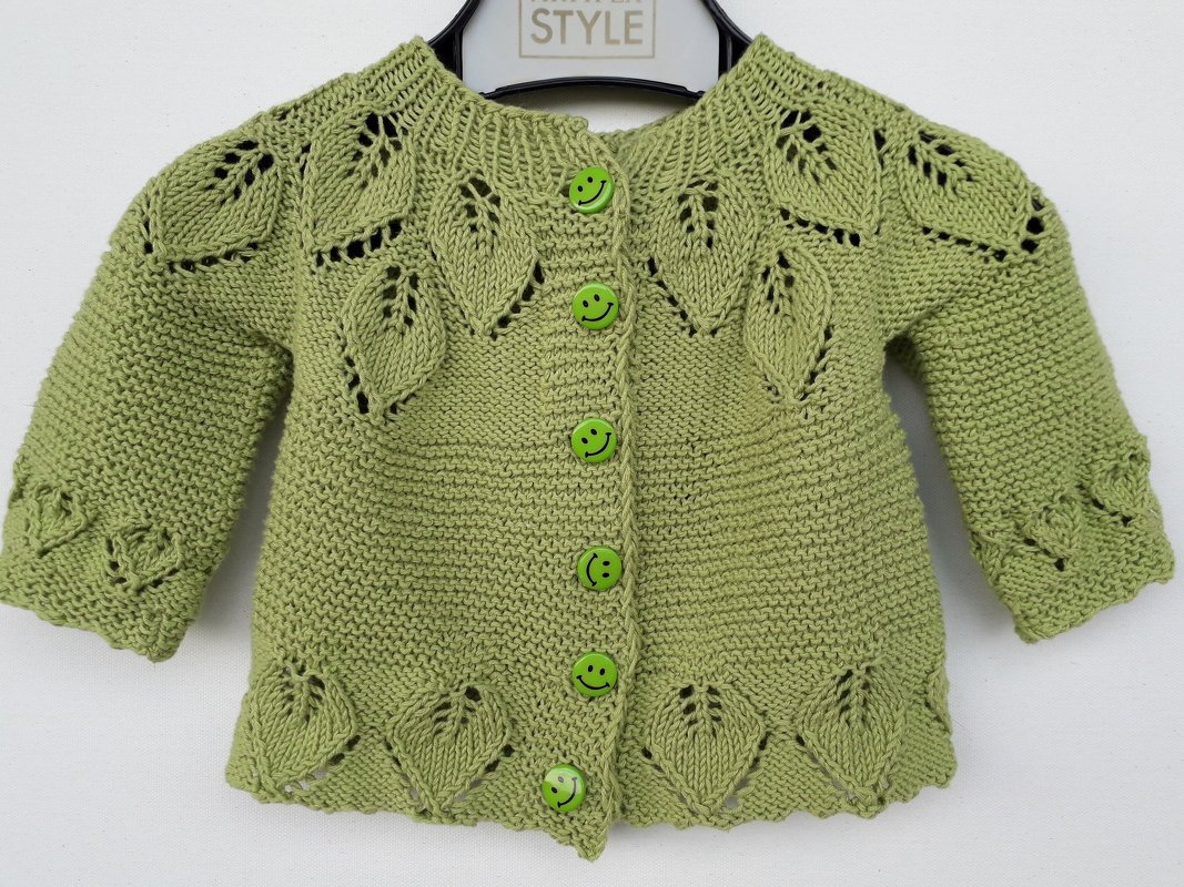 Hellgrüne gestrickte Babyjacke mit Ajour-Blättermuster an Schulter und Saum sowie sechs grünen Smiley-Knöpfen in der Mitte