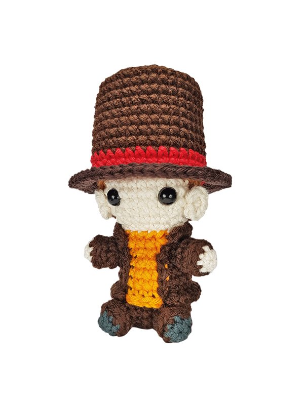Gehäkelte Amigurumi-Figur mit braunem Zylinderhut, rotem Hutband, braunem Mantel und orangefarbenem Oberteil vor weißem Hintergrund.