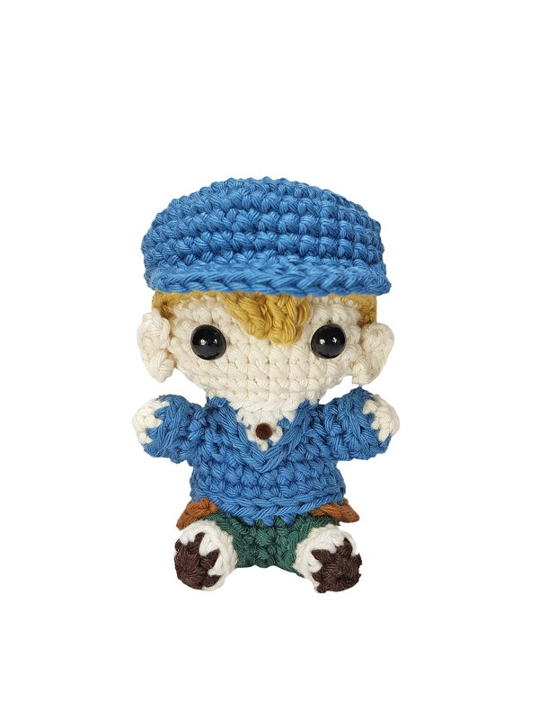 Gehäkelter Amigurumi-Junge mit blauer Mütze, blauem Pullover, grüner Hose und braunen Schuhen vor weißem Hintergrund