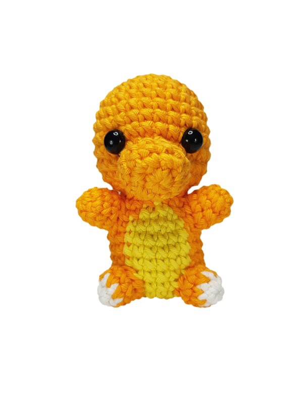 Gehäkeltes orange-gelbes Amigurumi-Drache mit schwarzen Augen und weißen Füßen vor weißem Hintergrund.