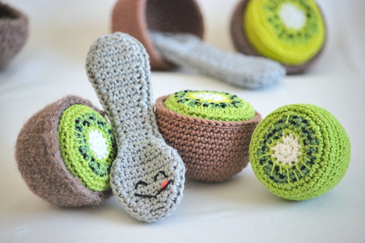 Gehäkelte Kiwihälften und ein grauer Löffel mit Gesicht aus Garn