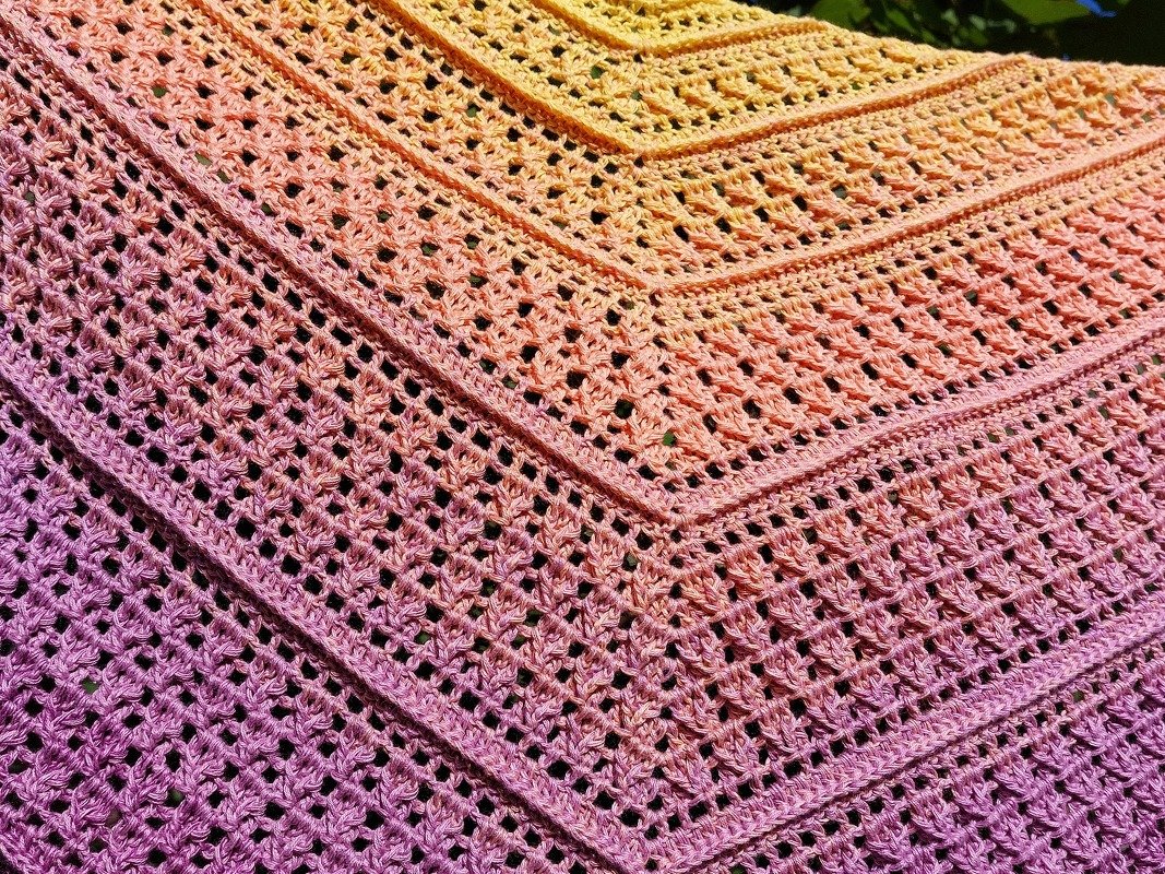 Crocheted triangle shawl with a gradient from yellow to purple, showing lacy openwork stitches and textured stitch bands.