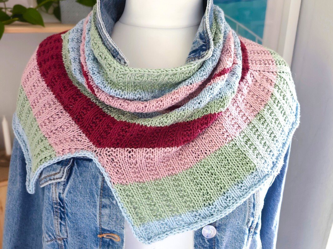 Gestrickter Dreiecksschal in Pastell- und Beerentönen auf Mannequin mit Jeansjacke
