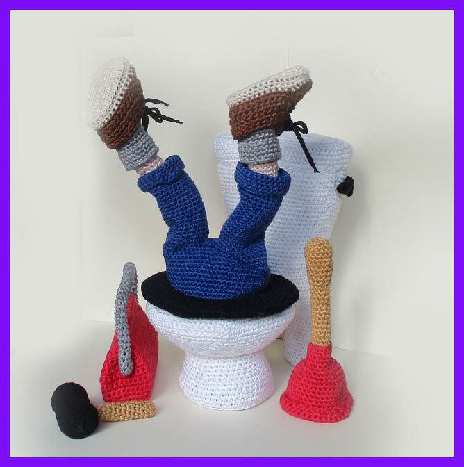 Gehäkelte Beine in blauen Hosen und Schuhen, die aus einer weißen Toilette ragen; daneben ein roter Pömpel und ein roter Reinigungsbehälter.