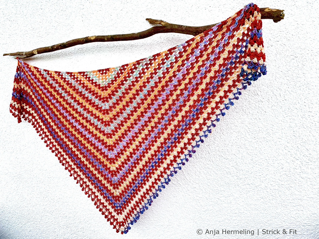 Striped granny-stitch triangle shawl in red, orange, purple and blue on a branch