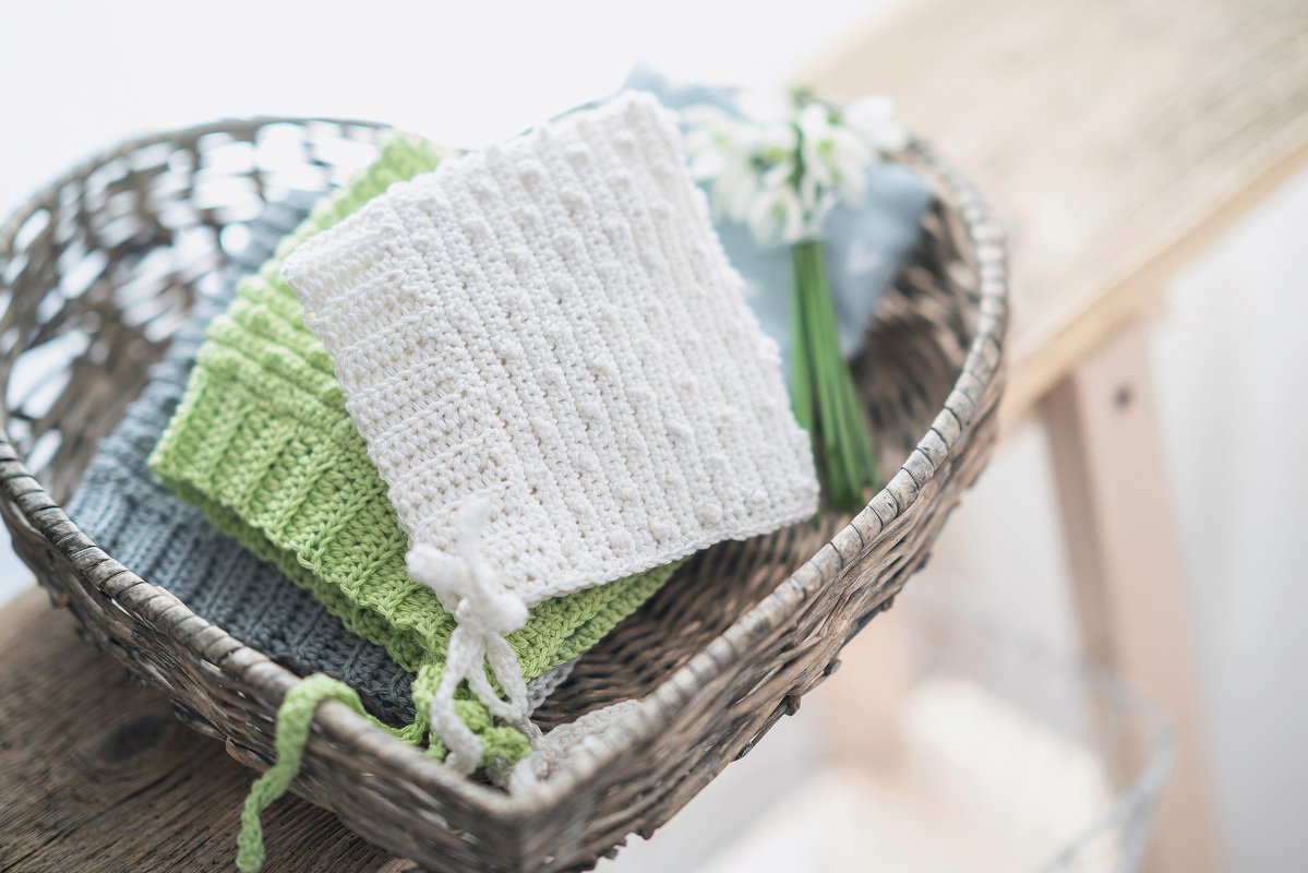 Gefaltete, handgehäkelte Babytücher in Weiß, Hellgrün und Grau in einem Weidenkorb
