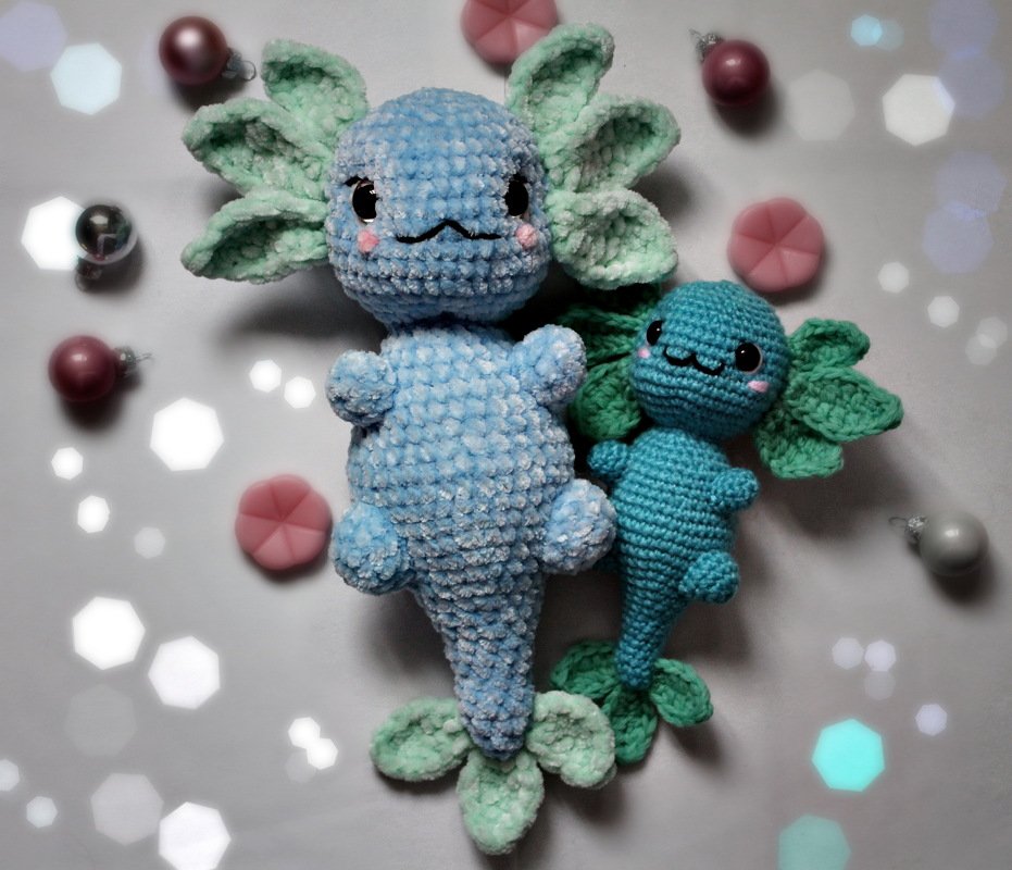 Zwei blaue gehäkelte Amigurumi-Wasserwesen mit fransigen Kiemen, liegend