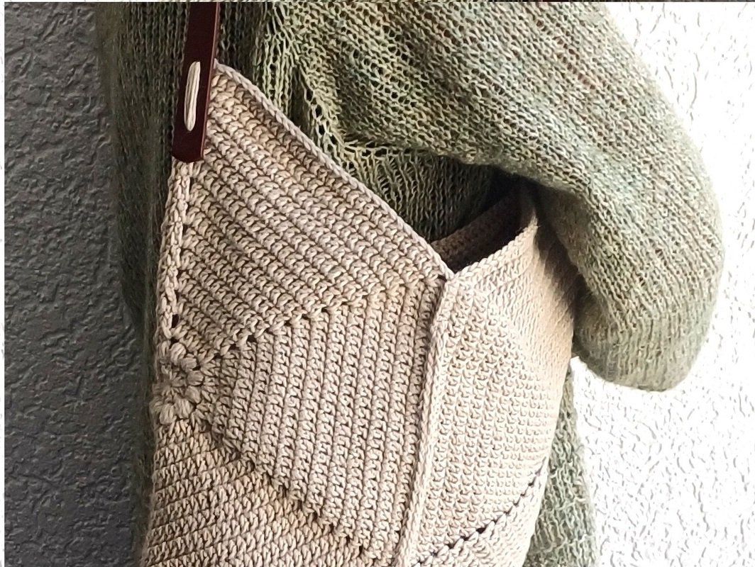 Beige gehäkelte Umhängetasche mit braunem Trageriemen, getragen über grünem Strickpullover