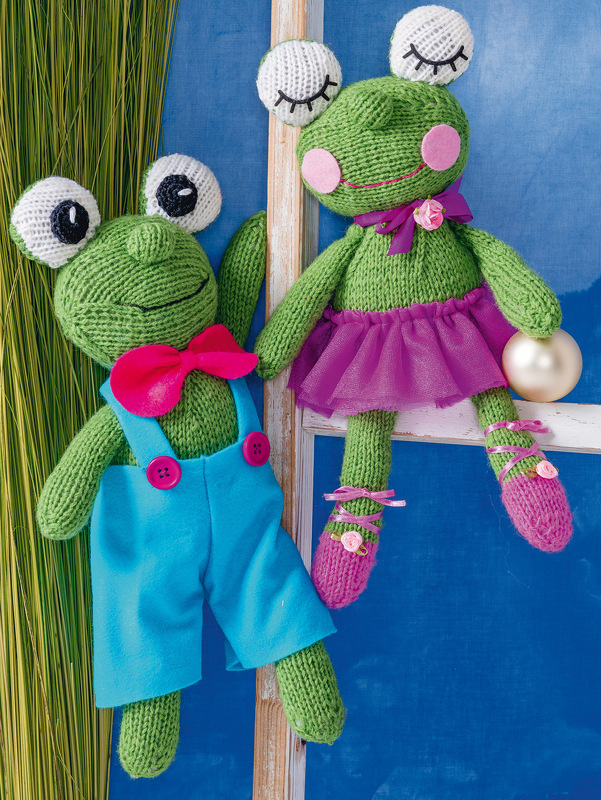 Zwei gestrickte grüne Amigurumi-Frösche, einer mit blauer Latzhose und Fliege, der andere mit violettem Tüllrock und Schlafaugen.