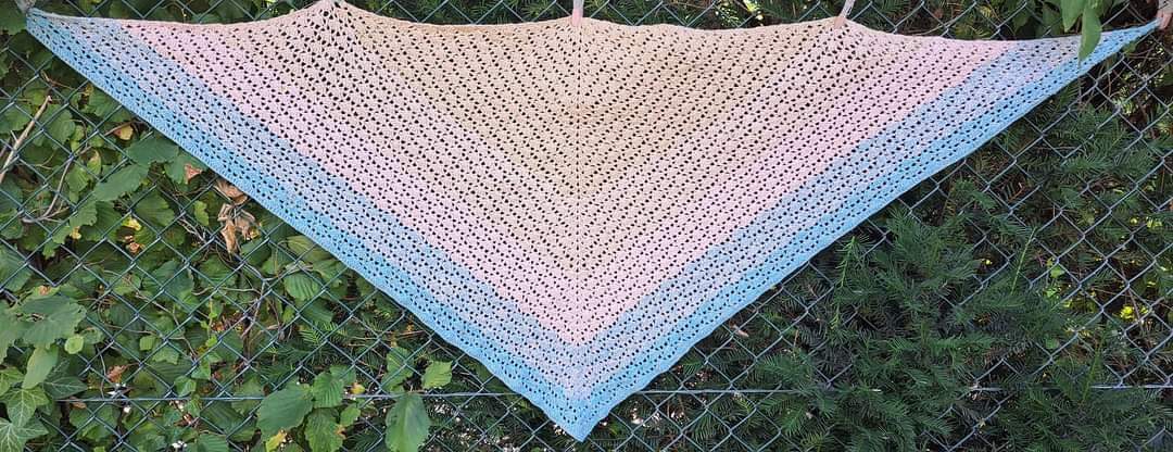Gehäkeltes Dreieckstuch in Pastellrosa zu Hellblau mit offenem Lochmuster, aufgehängt an Drahtzaun