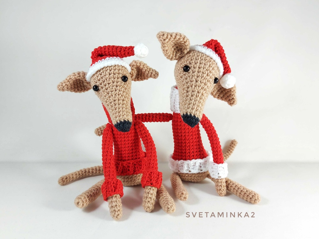 Two beige crocheted dog amigurumi wearing red Santa hats and sweaters, seated on a white background