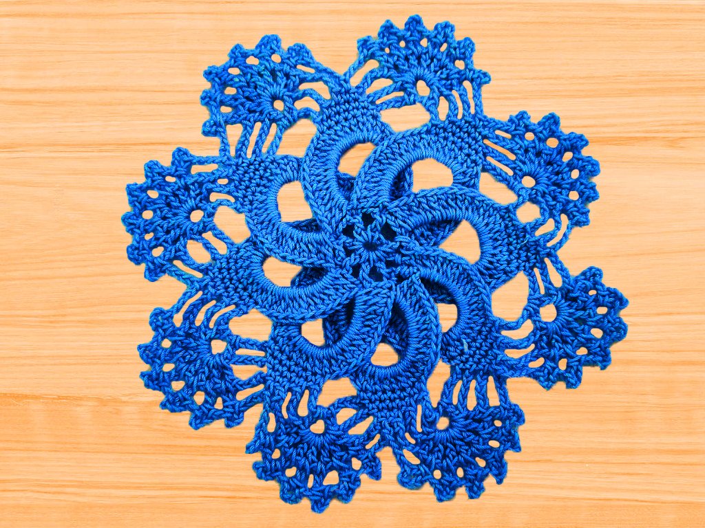 Blue crocheted round doily-style coaster with lacy floral pattern on wooden table