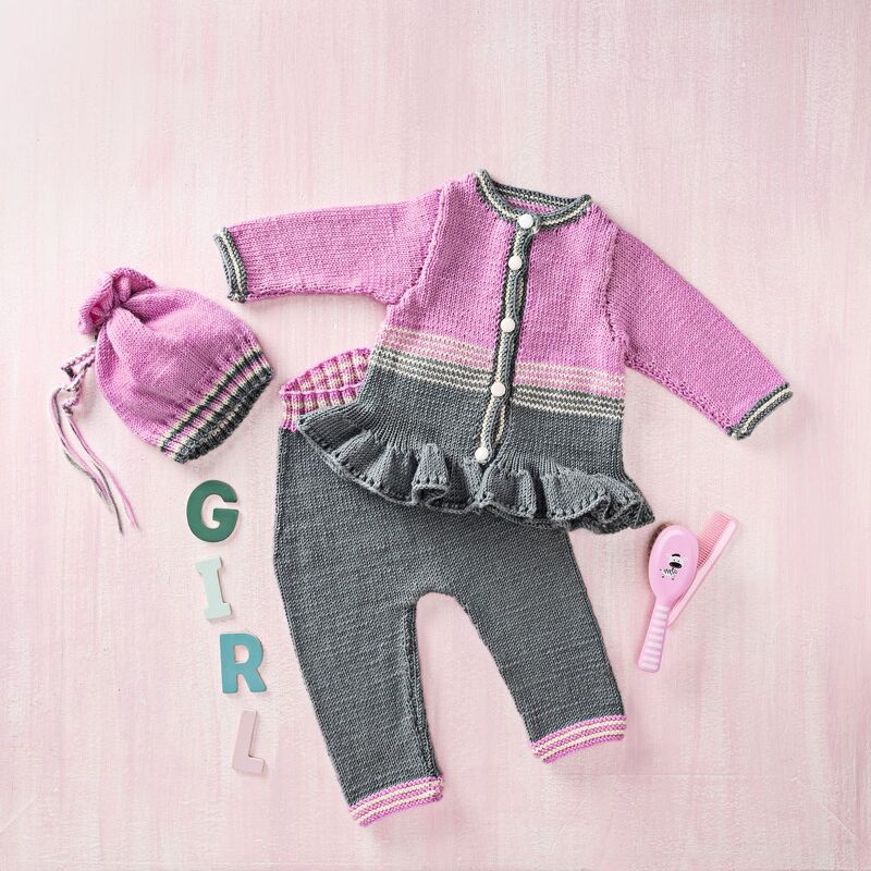 Gestricktes Babyset in Rosa und Grau mit Rüschenjacke, Hose und Beutel auf rosa Hintergrund, daneben Babybürste und Buchstaben G I R L