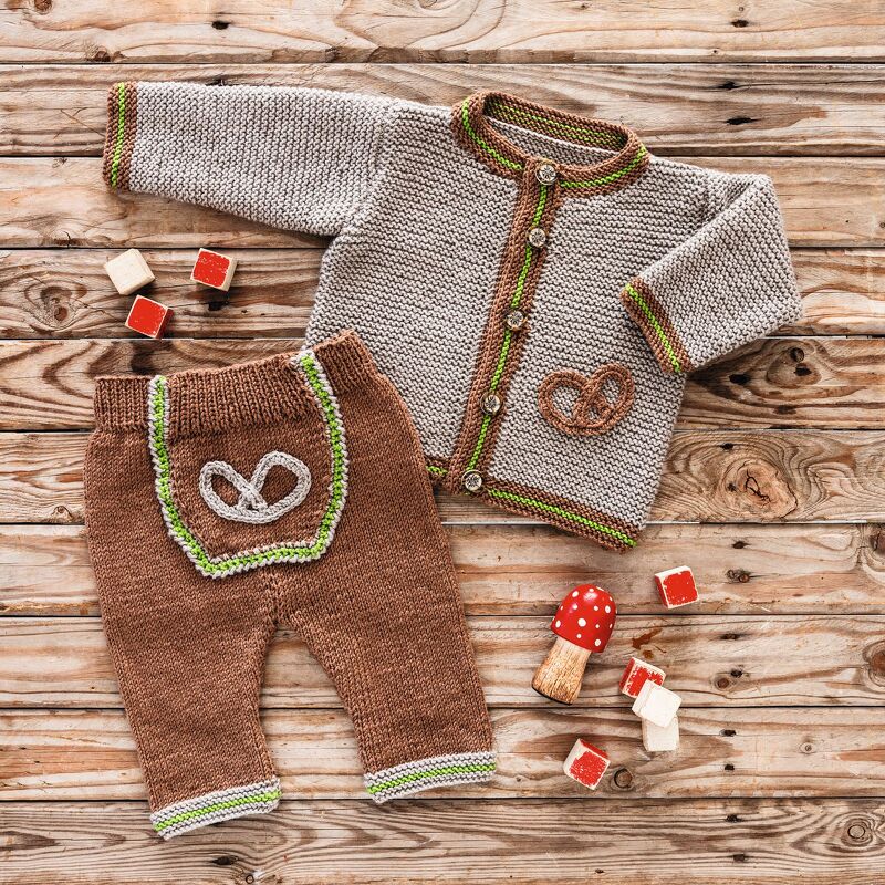 Gestrickte Babyjacke und Hose in Braun und Beige mit grünen Kontrastkanten und Brezel-Applikation auf Holzuntergrund
