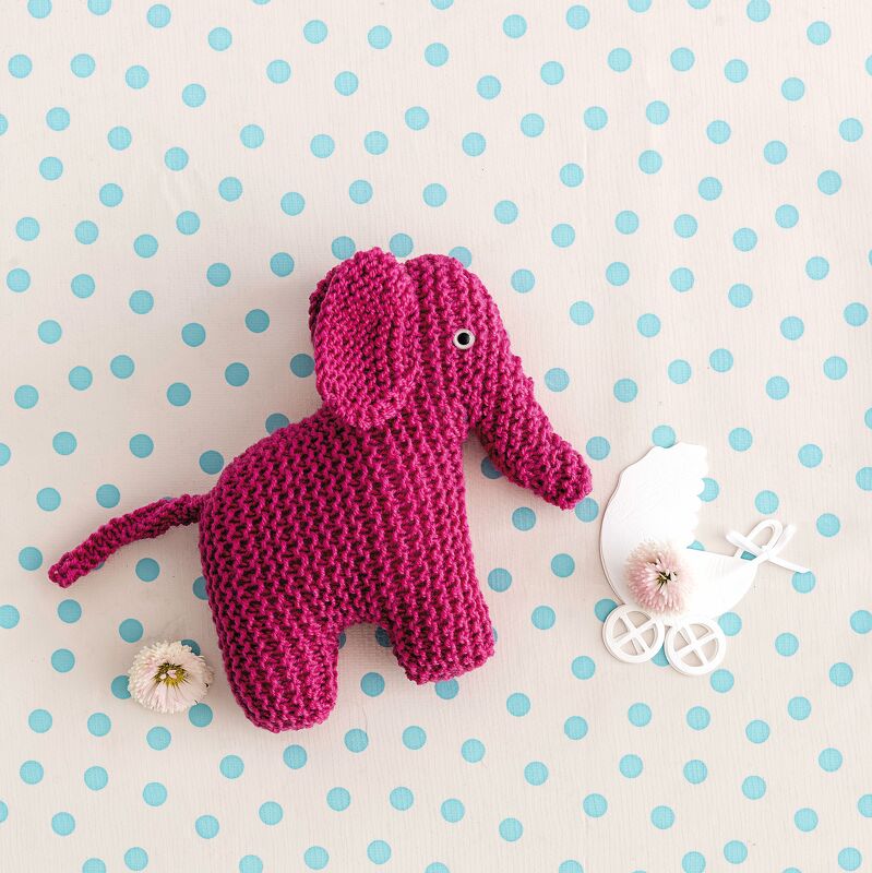 Detailaufnahme eines gestrickten fuchsienfarbenen Elefanten mit sichtbarer kraus‑rechts Maschenstruktur auf gepunktetem Untergrund