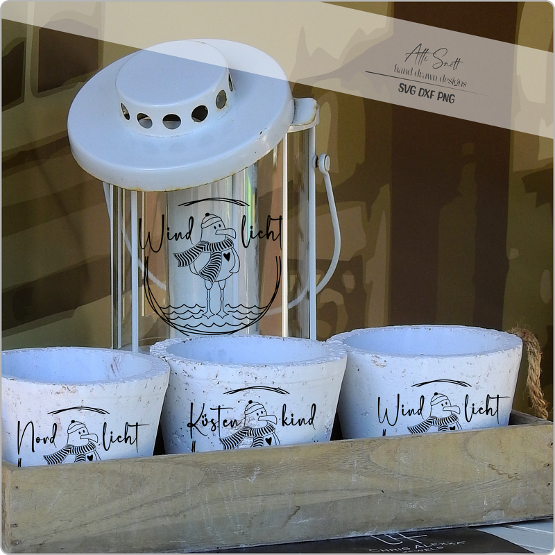 Weiße Laterne und drei weiße Tontöpfe mit schwarzem, maritimem Plotmotiv eines Vogels mit Mütze und den Schriftzügen Windlicht, Nordlicht und Küstenkind