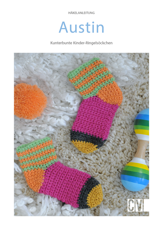 Zwei bunte gehäkelte Kinder-Ringelsöckchen in Pink, Orange, Grün und Gelb auf cremefarbenem Flausch, daneben eine Rassel und ein Bommel.