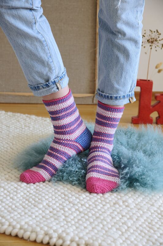 Gehäkelte, gestreifte Damensocken in Pink, Hellrosa und Violett mit blauer Ferse auf hellem Teppich