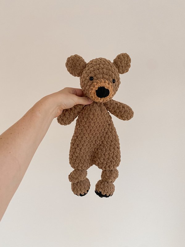 Close-up of a hand holding a brown crochet teddy bear to show stitch texture and limb joins
