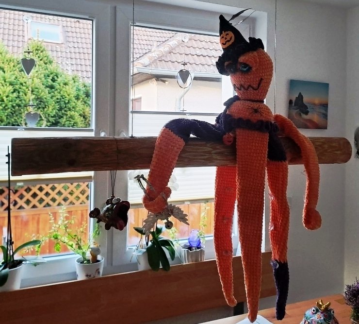 Gehäkelter orange-schwarzer Oktopus mit Hexenhut und Kürbis, hängend als Halloween-Dekoration