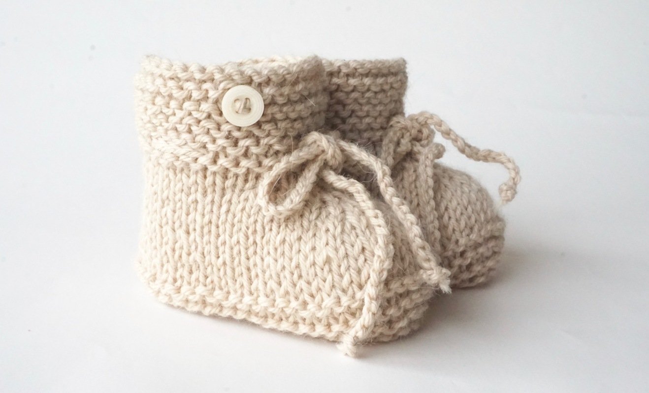 paar handgestrickter cremefarbener Babyschuhe mit Knopf und Schnürung