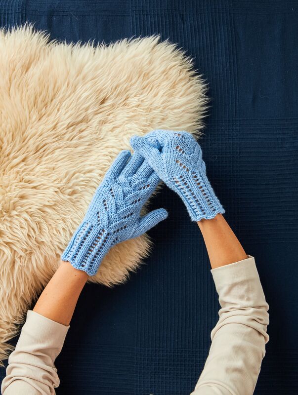 Hellblaue gestrickte Damenhandschuhe mit Loch- und Zopfmuster auf beigem Schaffellimitat und dunkelblauem Untergrund