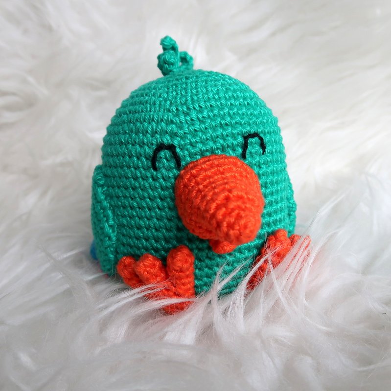 Gehäkelter türkiser Amigurumi-Vogel mit orangefarbenem Schnabel auf weißem Flausch