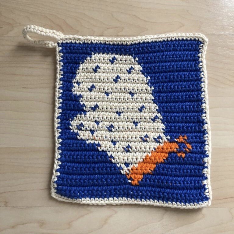 Quadratischer gehäkelter Topflappen in Dunkelblau mit cremefarbenem Handschuh-Motiv, orangefarbener Manschette und Eckschlaufe