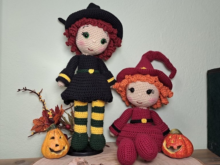 Zwei gehäkelte Amigurumi-Hexenpuppen mit Hüten neben kleinen Kürbis-Laternen