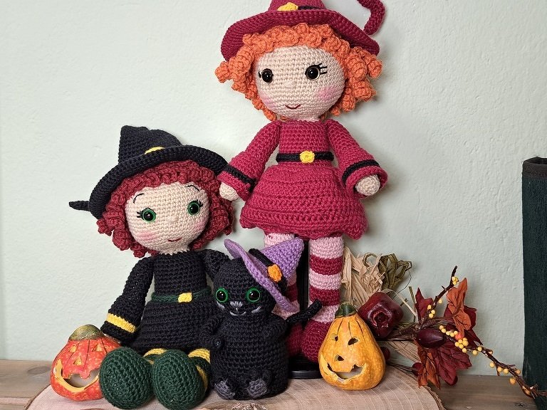 Zwei gehäkelte Amigurumi-Hexenpuppen und eine schwarze Katze als Halloween-Deko
