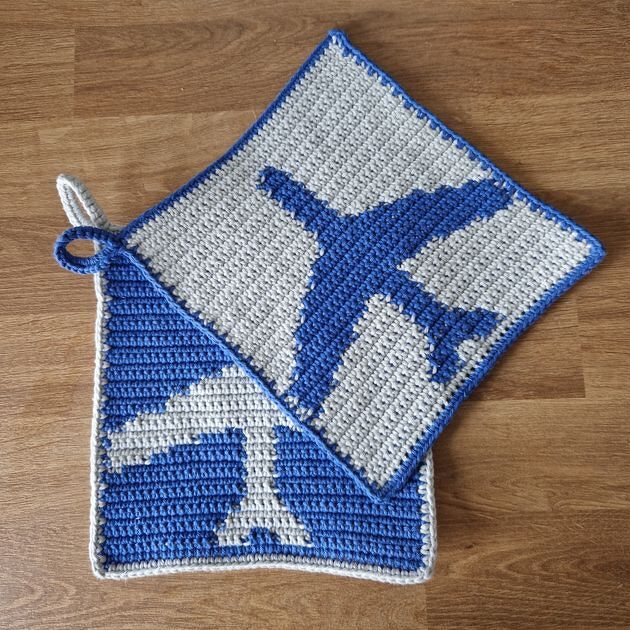 Zwei gehäkelte quadratische Topflappen mit invertiertem Flugzeugmotiv in Blau und Hellgrau auf Holzuntergrund