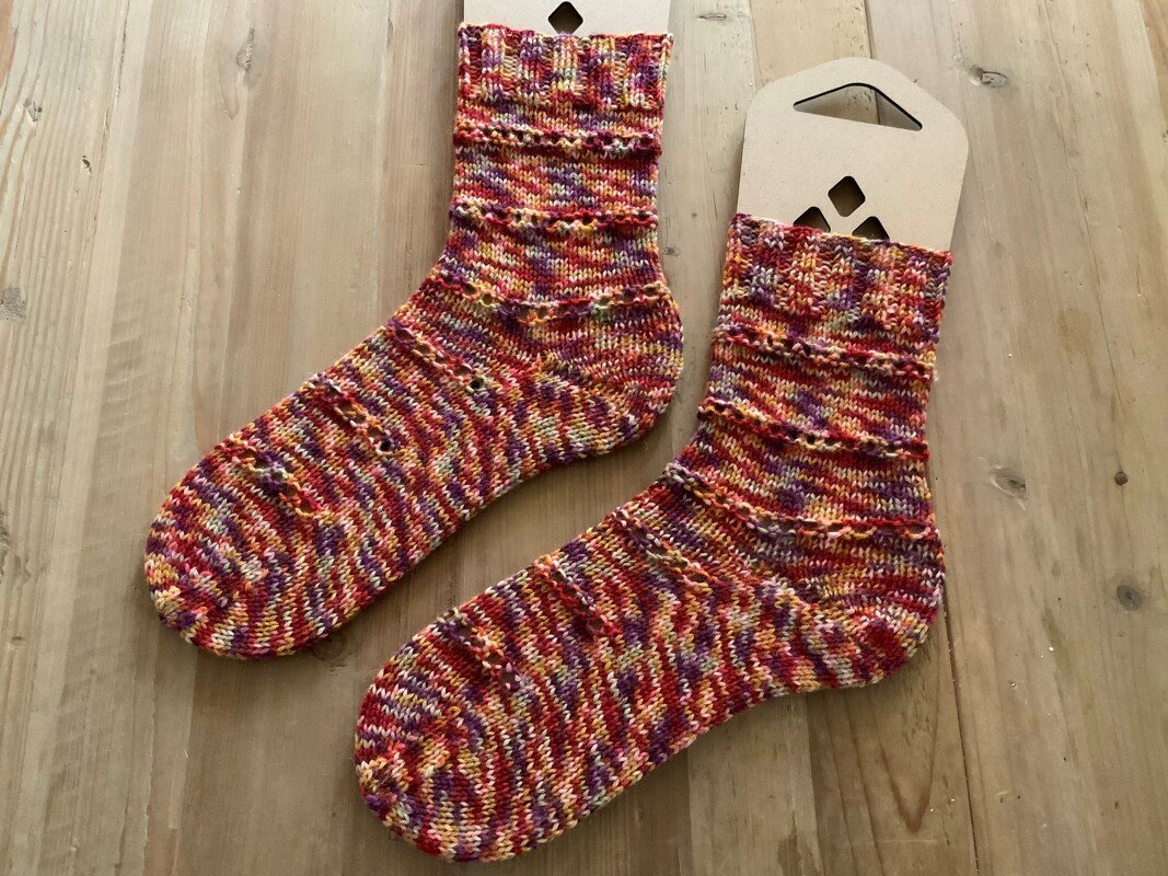 Handgestrickte mehrfarbige Socken in Rot, Gelb und Lila auf Holz mit Kartoneinlagen