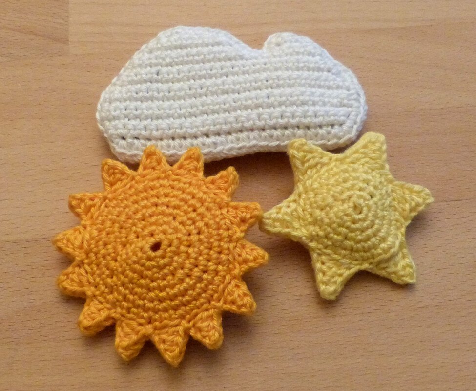 Weiße gehäkelte Wolke, gelber Stern und orangefarbene Sonne auf hellem Holzuntergrund