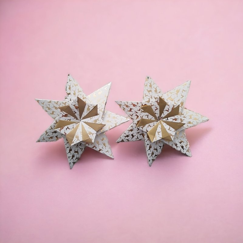 Zwei weiße Papiersterne mit goldenen Rentiermustern auf rosa Hintergrund