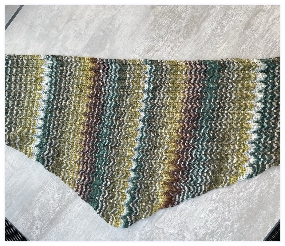 Gestricktes Dreieckstuch mit wellenförmigem Zickzack-Muster in Grün-, Braun- und Weißtönen auf hellem Untergrund.