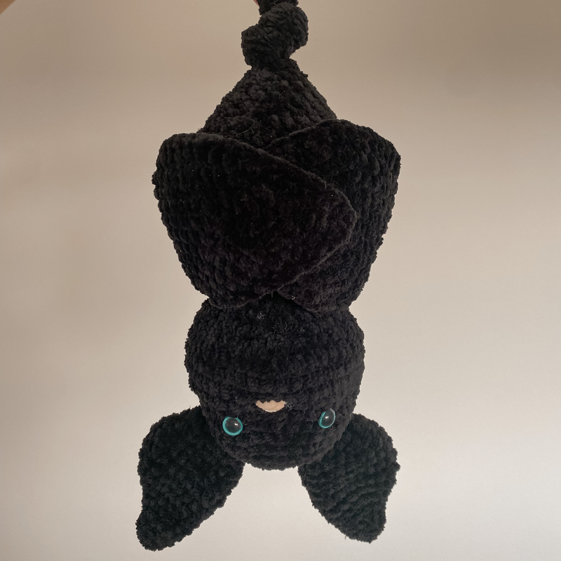Black crocheted bat amigurumi hanging upside down with teal safety eyes