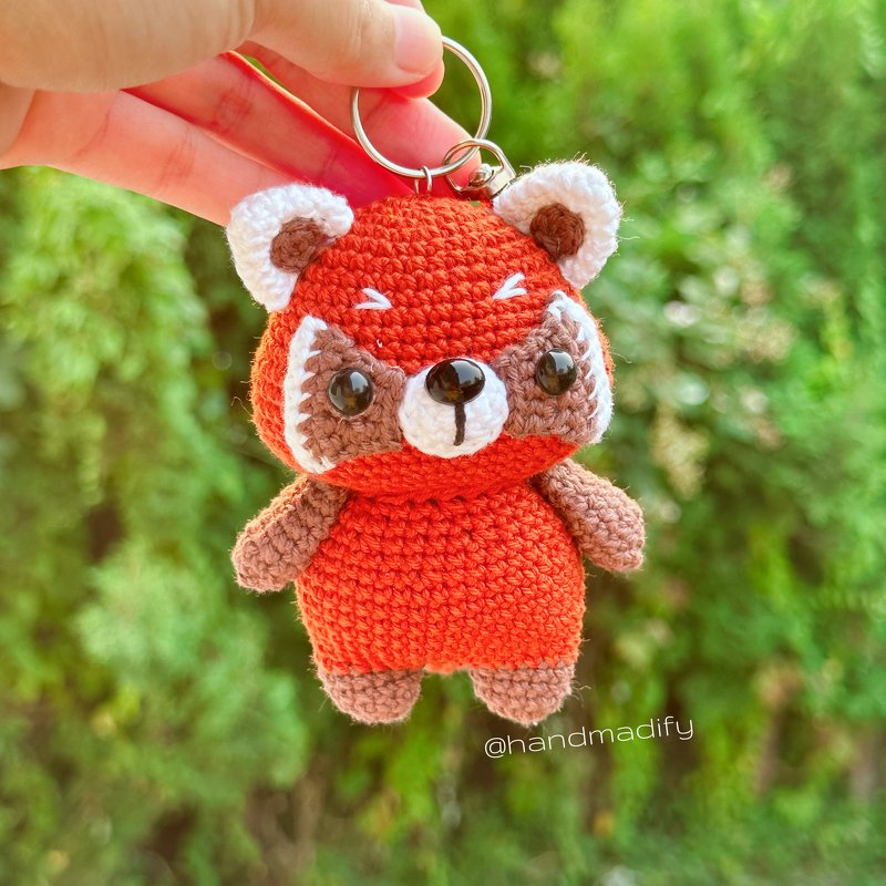Small crocheted red panda amigurumi keychain held by hand with green background
