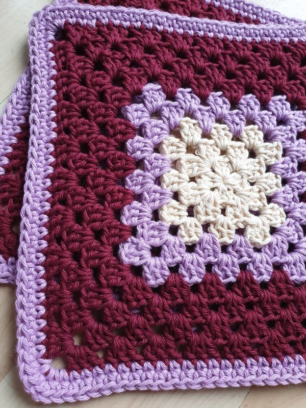 Crocheted granny square potholder with cream center, lilac rounds and burgundy body with lilac border