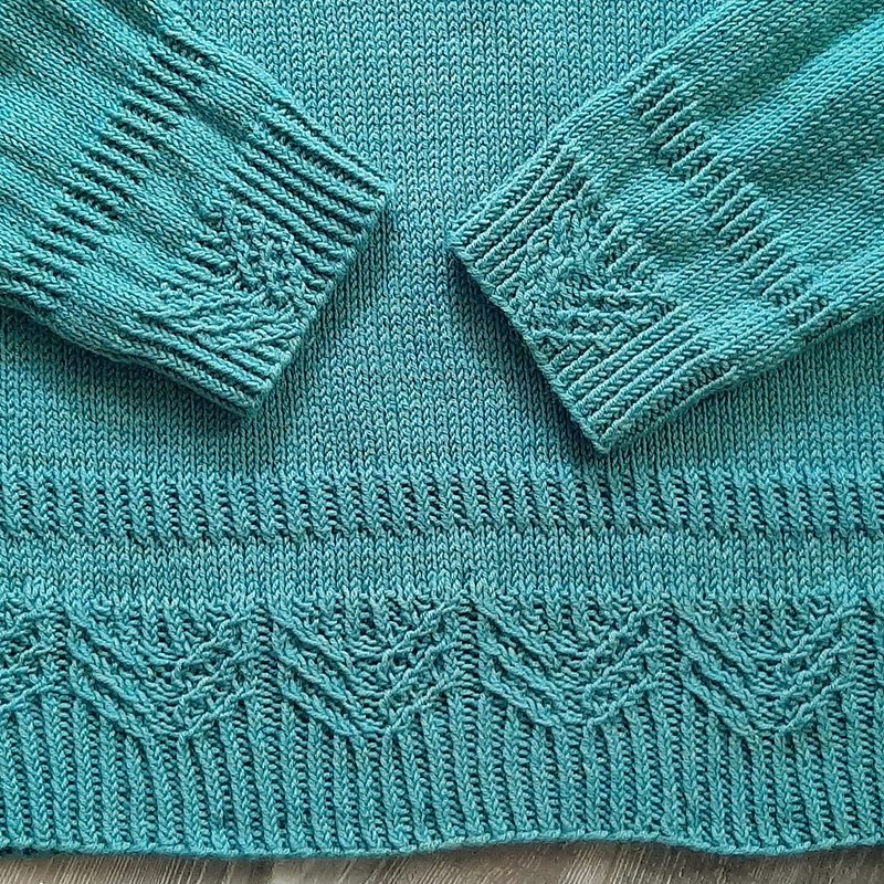 Nahaufnahme eines türkisen Strickpullovers mit Rippen-, Zopf- und Wellenmuster an Bündchen und Saum.