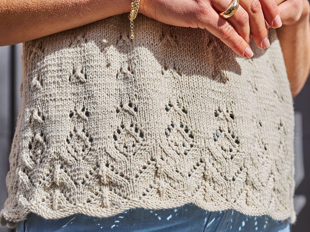 Detailaufnahme eines beigefarbenen gestrickten Damen-Tops mit Ajourreihen und gewelltem Saum