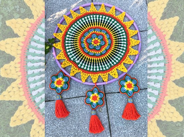 Gehäkelter Mandala-Traumfänger mit konzentrischen Mustern auf lila Ring und drei blütenförmigen Anhängern mit orangen Quasten