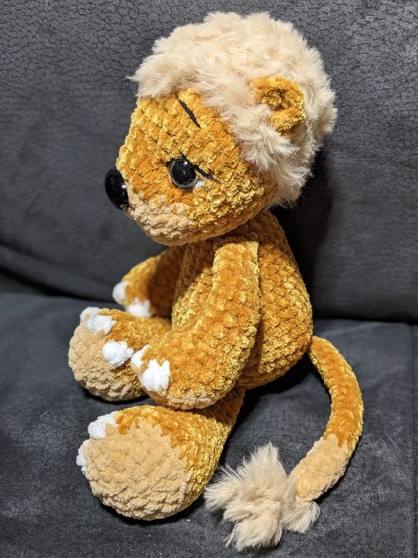 gelb‑beiger gehäkelter Amigurumi‑Teddy mit plüschiger Mähne und Schwanzquaste, seitliche Ansicht, sitzend