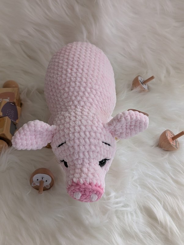 Nahaufnahme von oben eines rosa gehäkelten Amigurumi‑Schweinchens auf weißem Fell