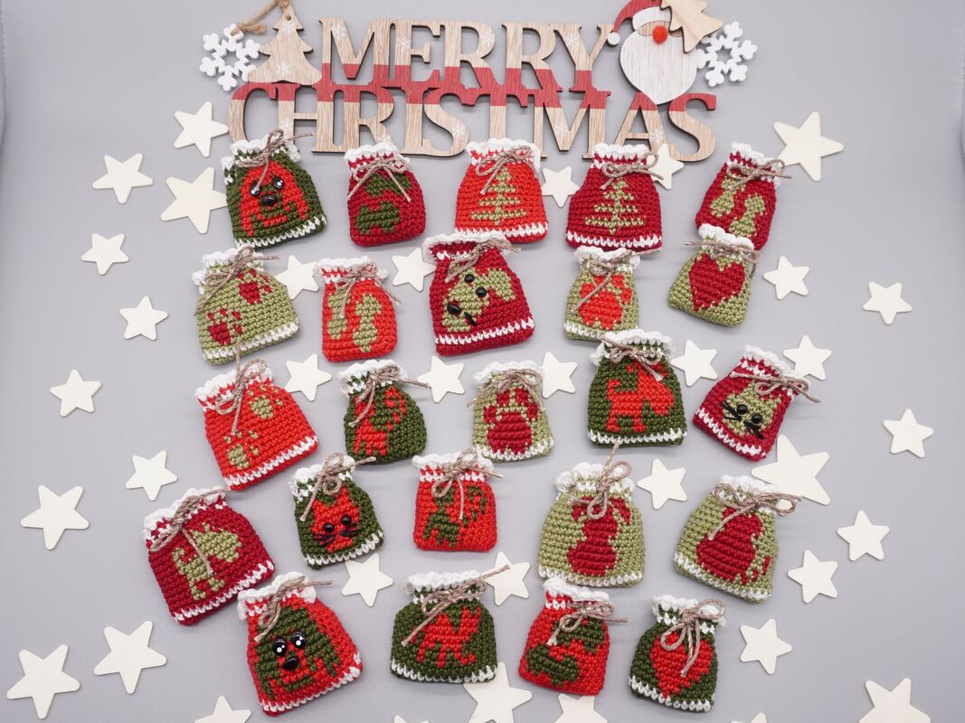 Nahaufnahme vieler kleiner rot-grüner gehäkelter Säckchen mit Weihnachtsmotiven, arrangiert um ein hölzernes Weihnachtsschild und weiße Sterne.