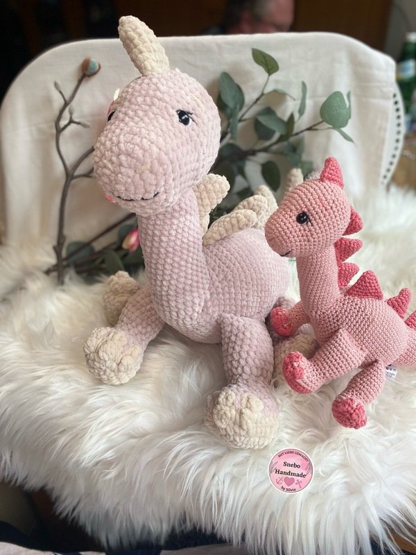 Zwei gehäkelte Amigurumi-Drachen in hell- und dunkelrosa auf flauschigem Untergrund