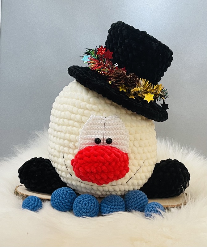 Gehäkelter Schneemannkopf mit roter Nase, schwarzem Zylinderhut und blauen Häkelbällen
