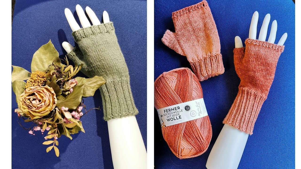 Gestrickte fingerlose Handschuhe in Grün und Lachs auf weißen Modellhänden, daneben ein Knäuel Wolle und Trockenblumen auf blauem Untergrund.
