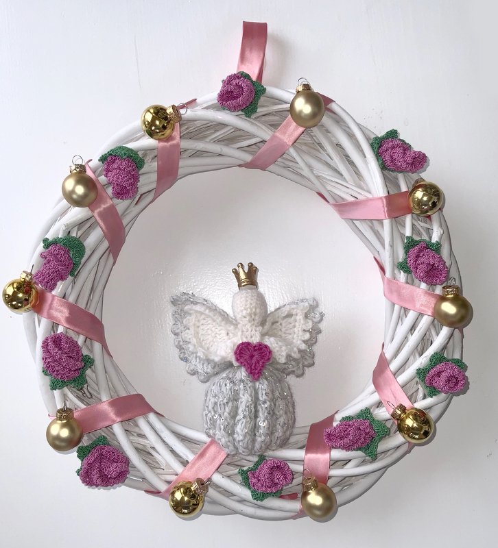 Weißer Türkranz mit gehäkeltem Engel, rosa Bändern, goldfarbenen Kugeln und kleinen Häkelrosen an weißer Wand