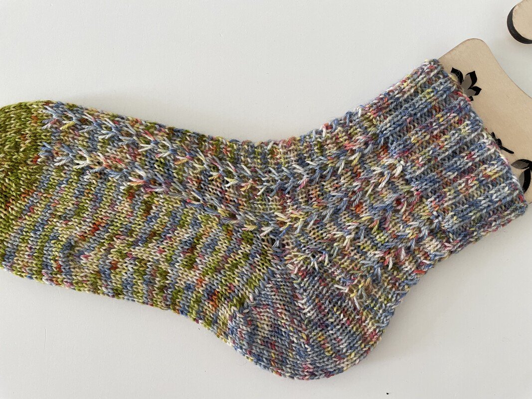 Mehrfarbige handgestrickte Socke mit Strukturmuster auf hellem Hintergrund.